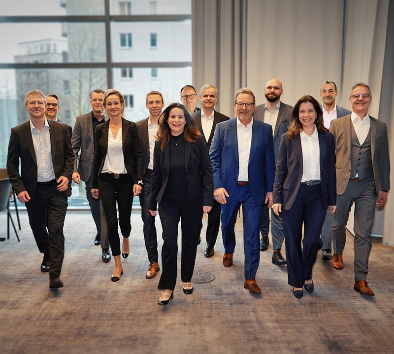 Eine Gruppe von Geschäftsleuten geht lächeln auf die Kamera zu.